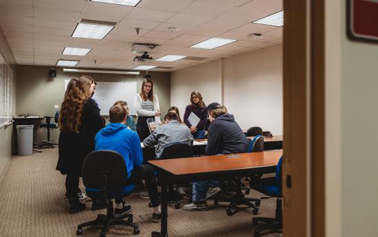 Several students gathered around a table where the instructor is showing blueprints in the architectural drafting and design course